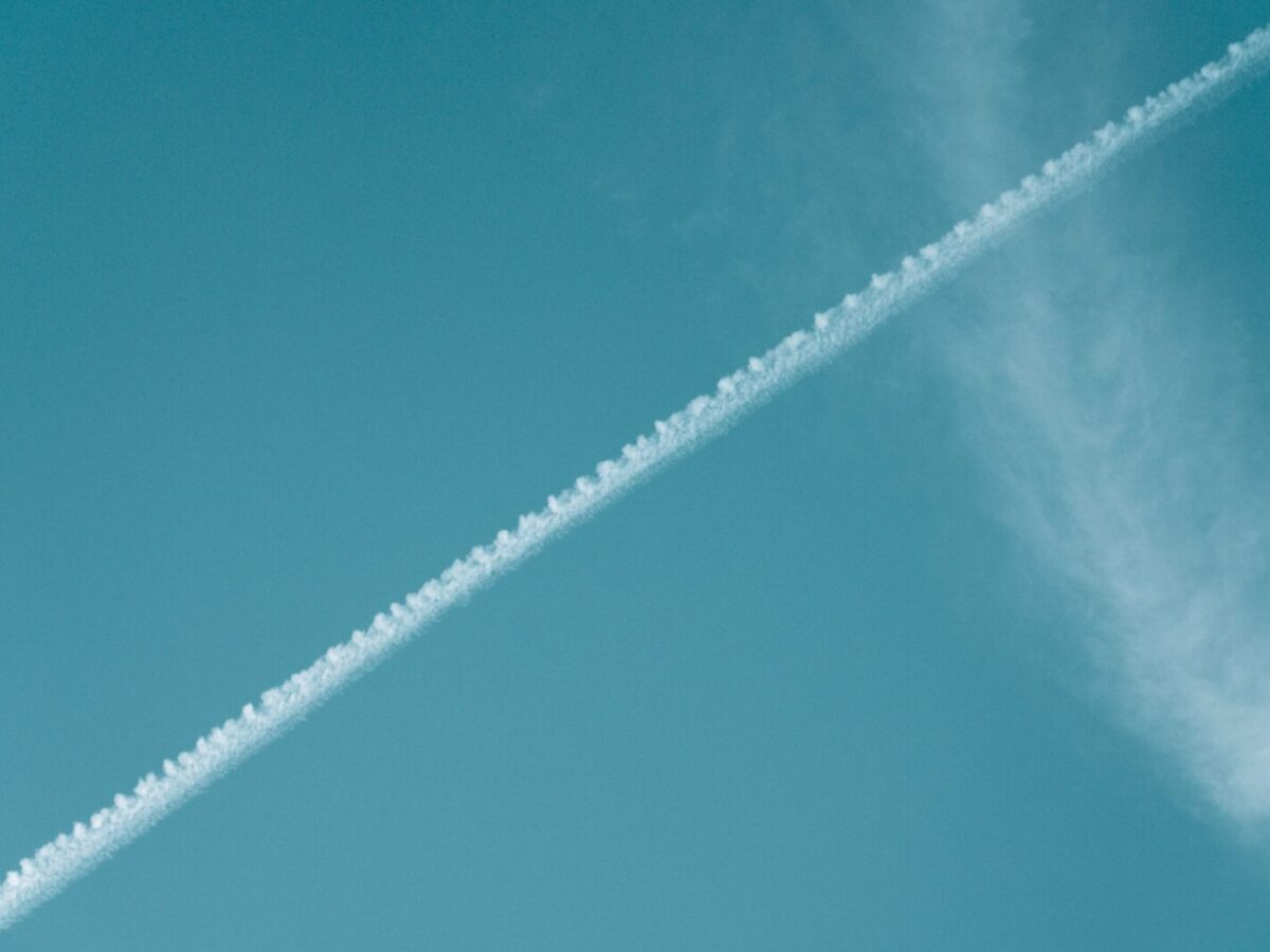 Airplane contrail streaking across a vibrant blue sky with wispy clouds.