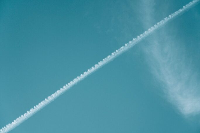 Airplane contrail streaking across a vibrant blue sky with wispy clouds.