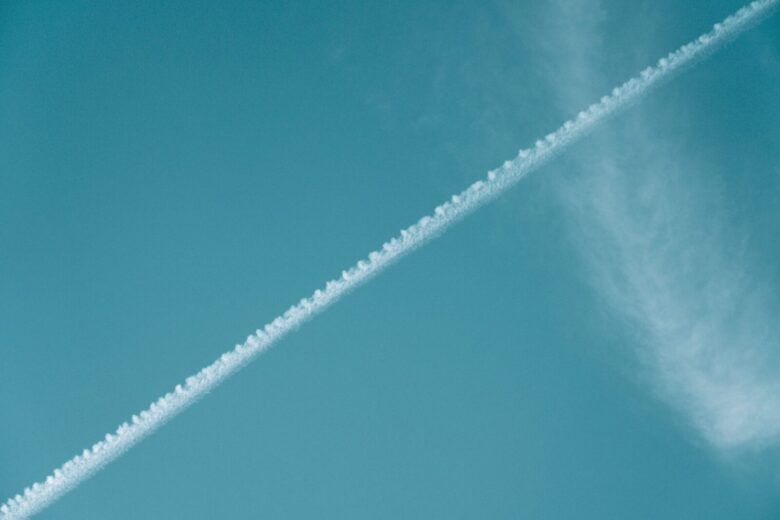 Airplane contrail streaking across a vibrant blue sky with wispy clouds.