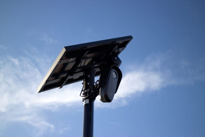 Sen. Warnock calls for guardrails around Flock surveillance camera use Solar-powered CCTV camera mounted on pole with bright sky background, symbolizing security and technology.
