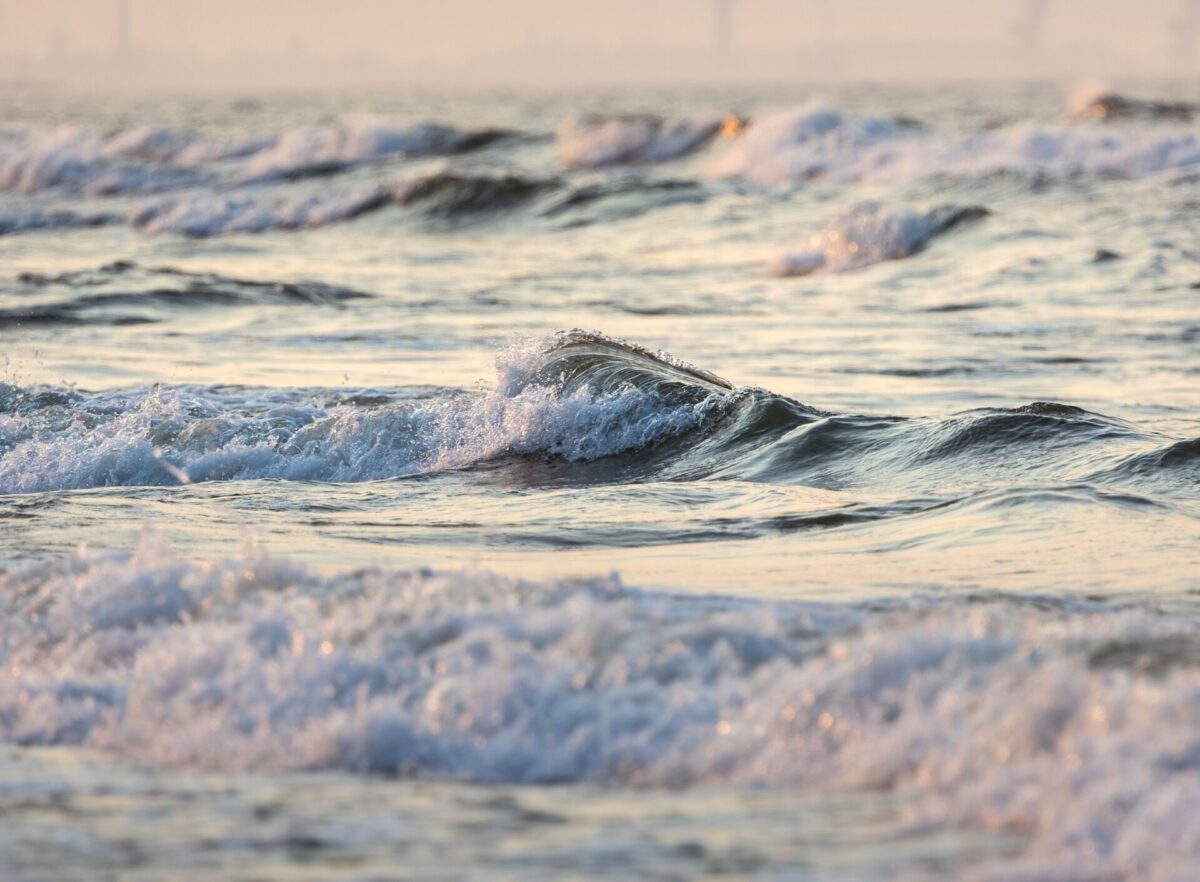 Gentle waves rolling onto a sandy shore at sunset on the Baltic Sea, reflecting golden hues.