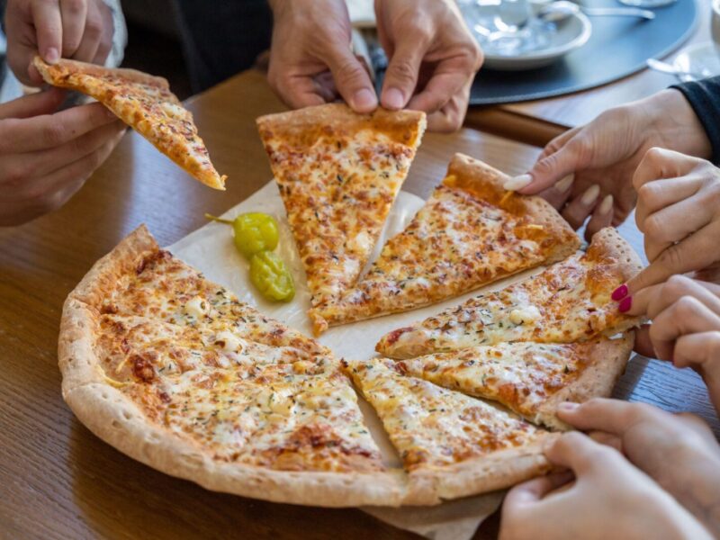 Multiple hands reaching for pizza slices on a cozy restaurant table.